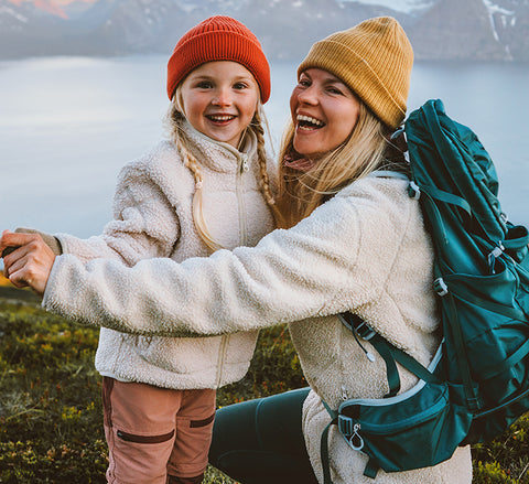 Woman and child in winter clothing with backpacks, standing in a snowy landscape.