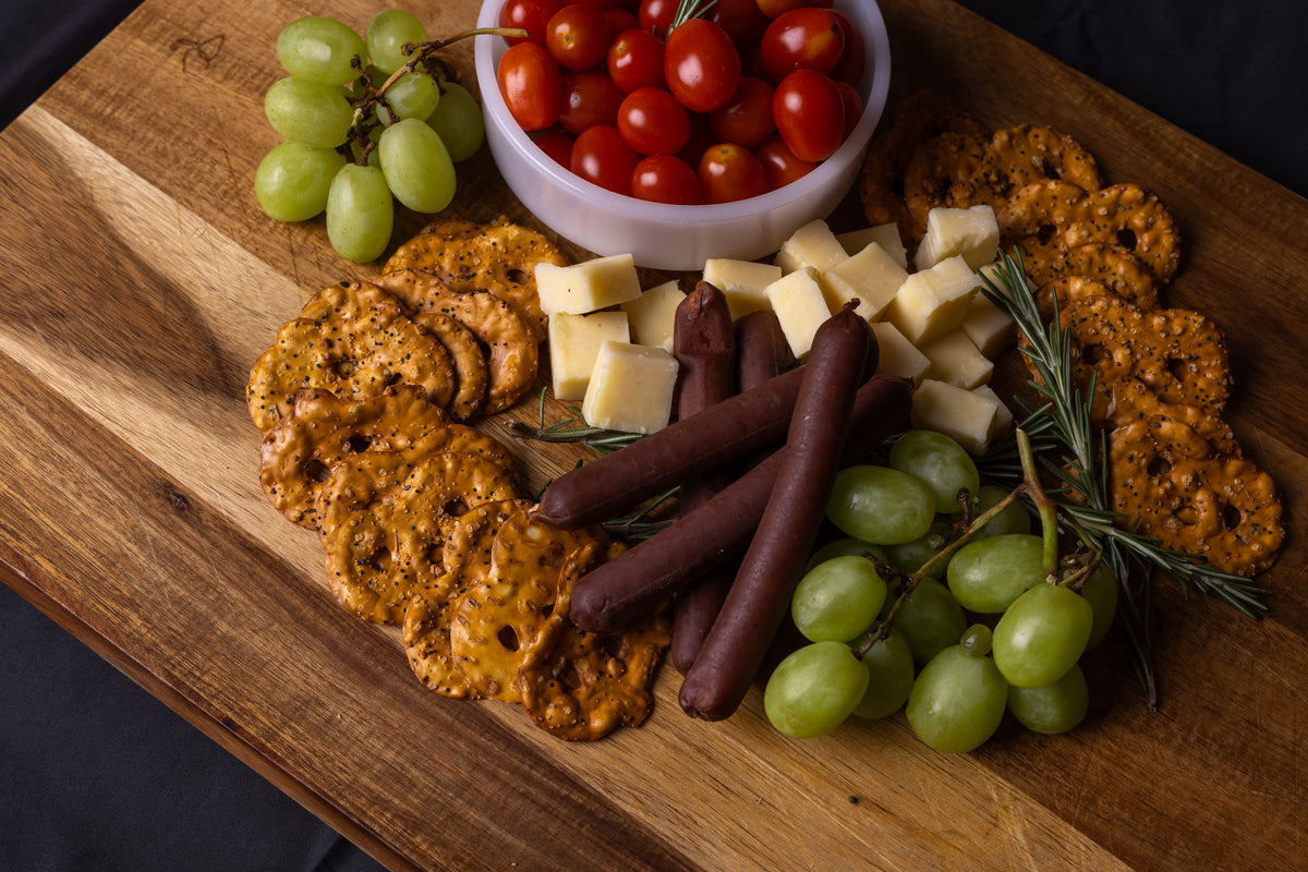 Wooden board with meat sticks, assorted cheeses, crackers, grapes, and cherry tomatoes.